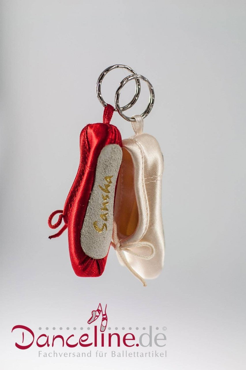 Vor einem weißen Hintergrund sind zwei Miniatur-Ballettschuh-Schlüsselanhänger abgebildet. Ein Mini-Spitzenschuh-Anhänger Sansha KRPS Minipoint ist rot mit der Aufschrift „Bambi“ auf der Sohle, der andere ist elfenbeinfarben. Unten im Bild ist der Text „Danceline.de Fachversand für Ballettartikel“ zu sehen.
