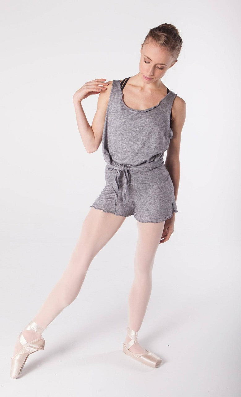 Eine Tänzerin trägt einen grauen Leotard mit passendem Gürtel, weiße Strumpfhosen und rosa Ballettschuhe und nimmt eine selbstbewusste Ballettpose mit leicht zur Seite geneigtem Kopf ein. Ihr Outfit umfasst unter dem Leotard die Hose Intermezzo 5213 Nacurt von Intermezzo für zusätzlichen Komfort. Der Hintergrund ist schlicht weiß.