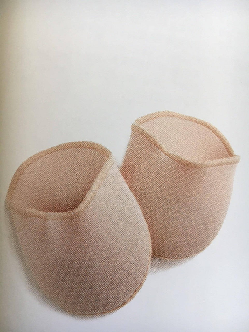 Zwei hellrosa, halbrunde Zehenpolster aus Stoff, bekannt als Zehenpolster Bunhead BH005 OuchPouch von Dance Line, sind nebeneinander vor einem weißen Hintergrund platziert. Jedes Polster ist an einem Ende offen und scheint gepolstert zu sein, wahrscheinlich für den Einsatz in Tanzschuhen für zusätzlichen Komfort und Schutz konzipiert.