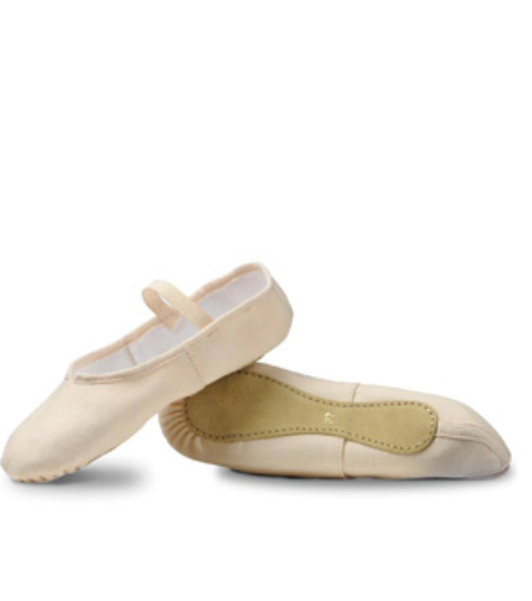 Ein Paar beige Ballettschuhe Merlet Envol mit leichtem Glanz, perfekt für Kinder oder Anfänger. Ein Schuh liegt flach auf der Oberfläche, während der andere darauf balanciert, wodurch die Struktur der Unterseite und das Sohlendesign sichtbar werden. Der flache Schuh verfügt über einen elastischen Riemen an der Oberseite für einen sicheren Sitz.