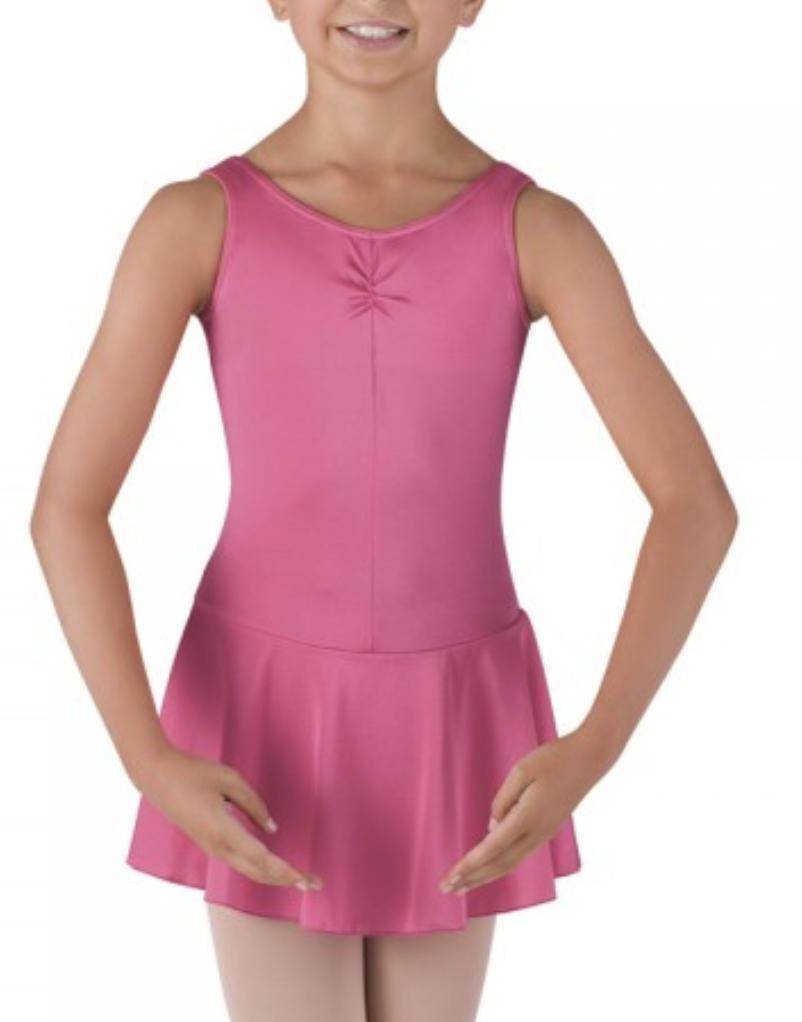 Eine junge Person in einem rosa Kinder Ballettanzug Bloch BU902C mit angenähtem Rock steht mit gerundeten Armen auf Taillenhöhe und trägt beige Strumpfhosen. Der Hintergrund ist schlicht weiß.