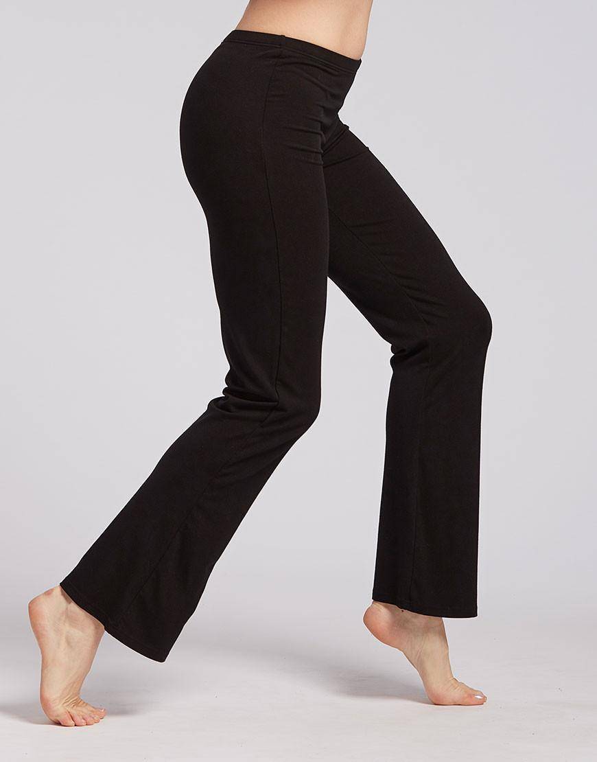 Eine Person, die die schwarze Yogahose Jazzhose TempsDanse Luna von Temps Danse trägt, steht auf den Zehenspitzen, wobei das linke Bein leicht gebeugt und das rechte Bein gestreckt ist. Der Hintergrund ist schlicht und hell, was die Dehnbarkeit und Flexibilität der Hose hervorhebt.