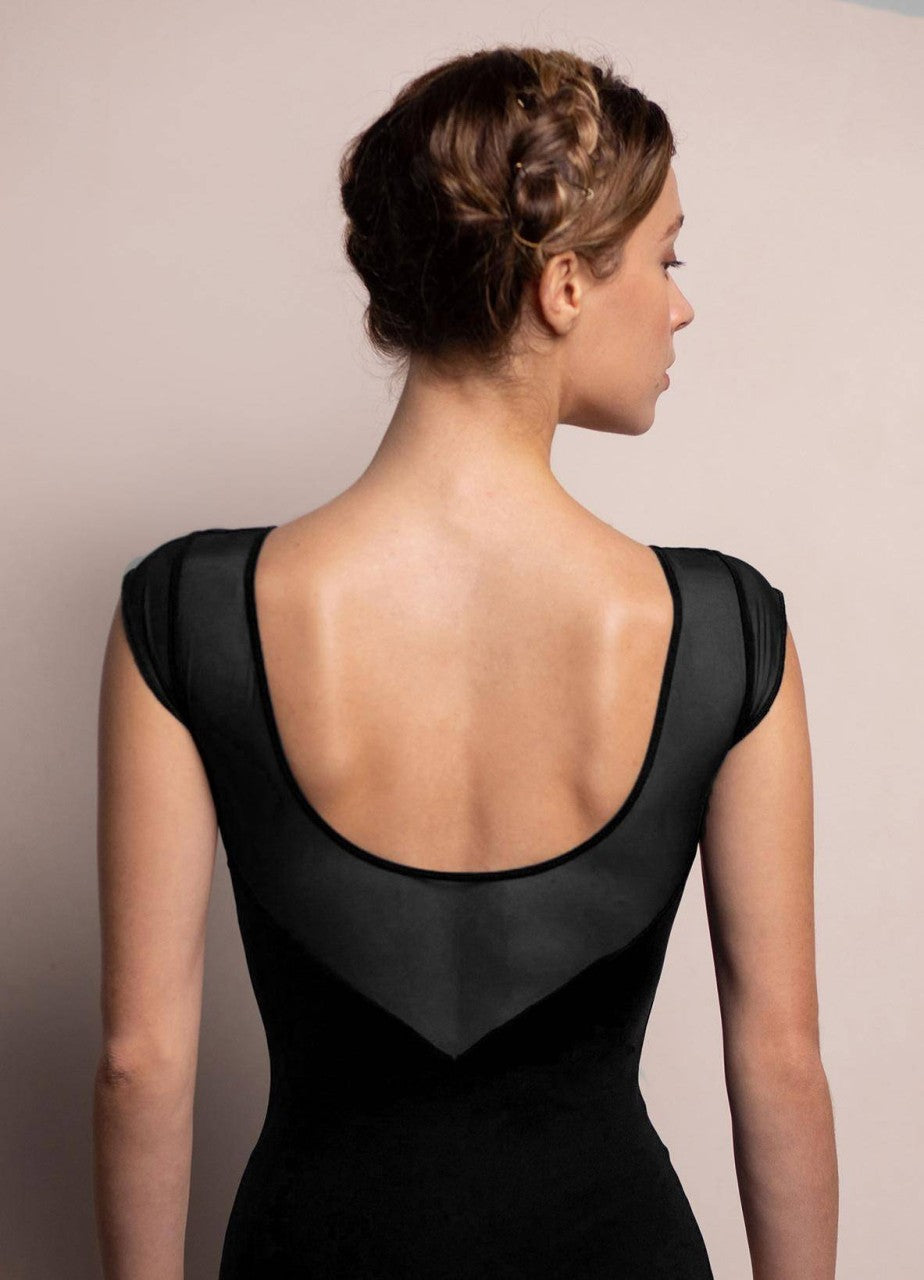 Eine Frau mit geflochtenen braunen Haaren ist von hinten zu sehen. Sie trägt den Intermezzo Ballettanzug 31547 Mesh, ein schwarzes Kleid mit tiefem Rückenausschnitt und zarten Netzdetails. Sie steht vor einem einfachen zweifarbigen Hintergrund in neutralen Farben.