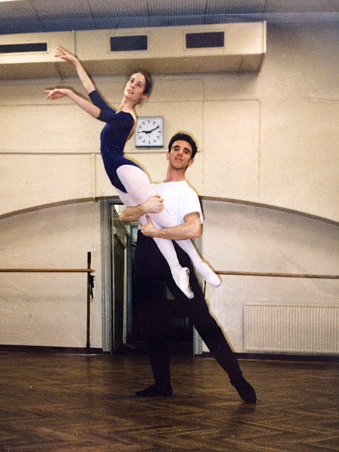 Eine Pas de Deux Pose im Ballettsaal. Ein Balletttänzer hält die Beine der Ballerina und sie hat die Arme elegant in der 3. Armposition.