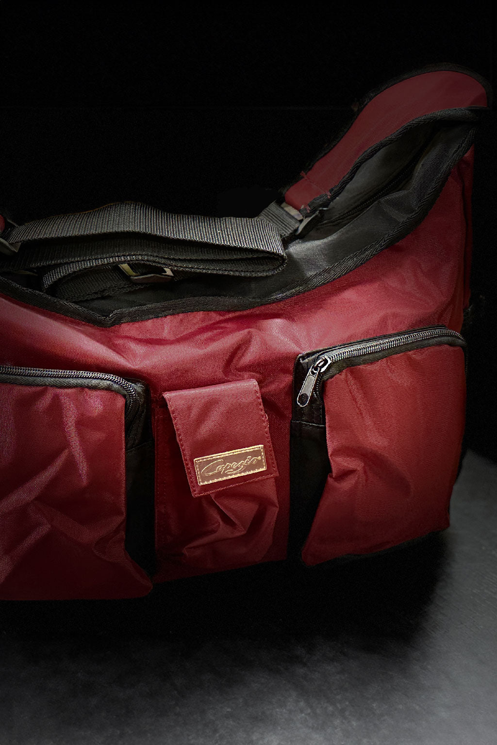 Die Ballett Tasche Capezio 56B Slim Duffle von Capezio, eine rote gepolsterte Tasche mit zwei Reißverschlusstaschen und einem Schultergurt, ist auf einem dunklen Hintergrund abgesetzt. Auf der Vorderseite ist ein kleines Logo sichtbar.