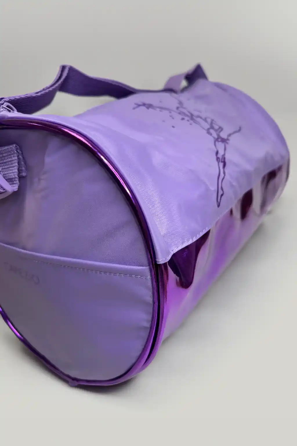 Die Balletttasche Capezio Cosmo B277 von Capezio ist eine zylindrische Reisetasche mit einem violetten Hochglanzfinish und einer aufgedruckten Grafik auf der Oberseite. Sie verfügt über einen Schultergurt und einen Reißverschluss an der Seite, der aufrecht auf einem hellgrauen Hintergrund steht.