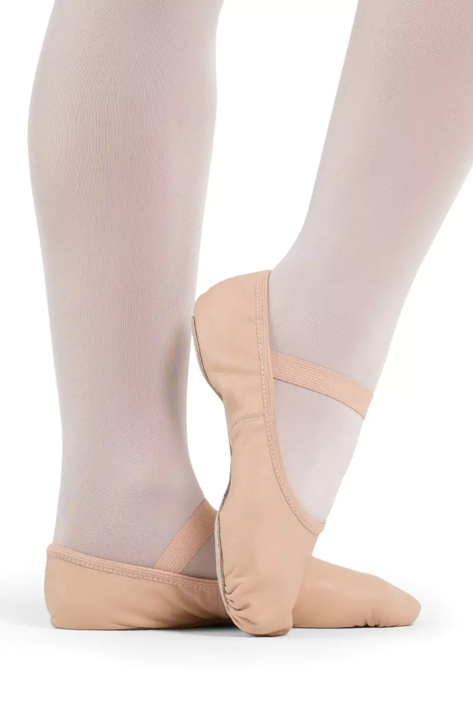 Eine Person in weißer Strumpfhose und den Capezio Ballettschuhen V100 Luna in Beige steht in einer Ballettpose vor einem schlichten Hintergrund. Die Schuhe haben oben elastische Riemen.