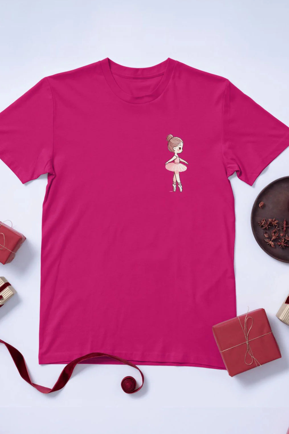 Das Ballett T-Shirt Danceline Little Ballerina von Dance Line ist ein rosa Shirt mit einem kleinen Cartoon-Balletttänzer-Motiv auf der linken Brust. Das Motiv ist umgeben von kleinen Geschenkboxen, Bändern, einem Teller mit Sternanis und einem roten Ball, alles auf einem hellen Untergrund.