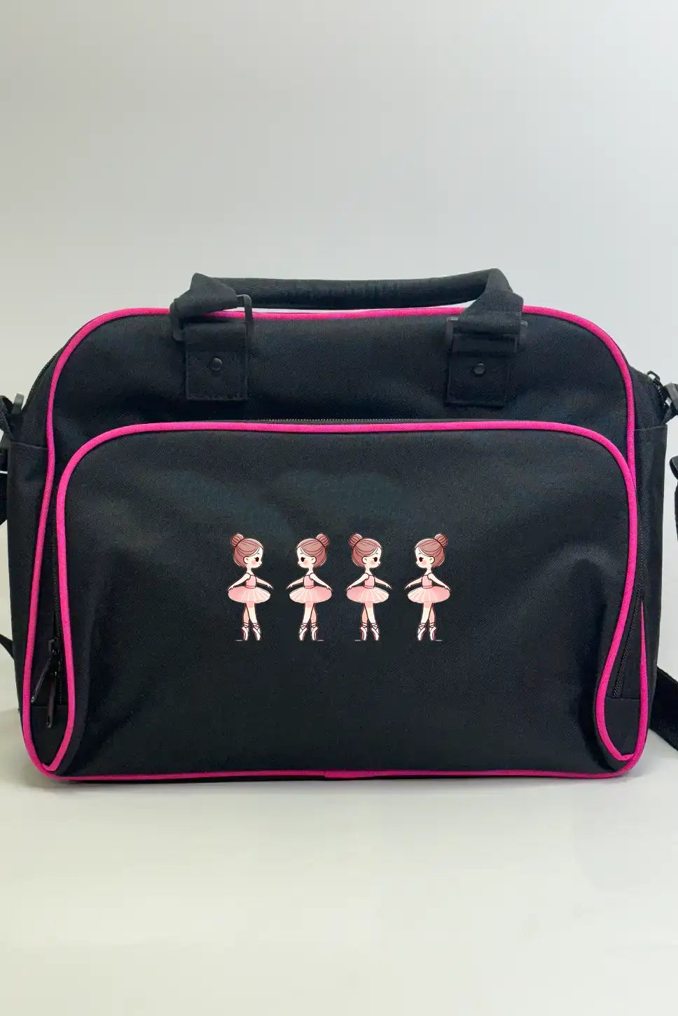 Die Danceline Kinder Balletttasche ist eine schwarze Umhängetasche mit rosa Paspelierung und einem gestickten Design von vier Ballerinas in rosa Kleidern auf der Vordertasche.