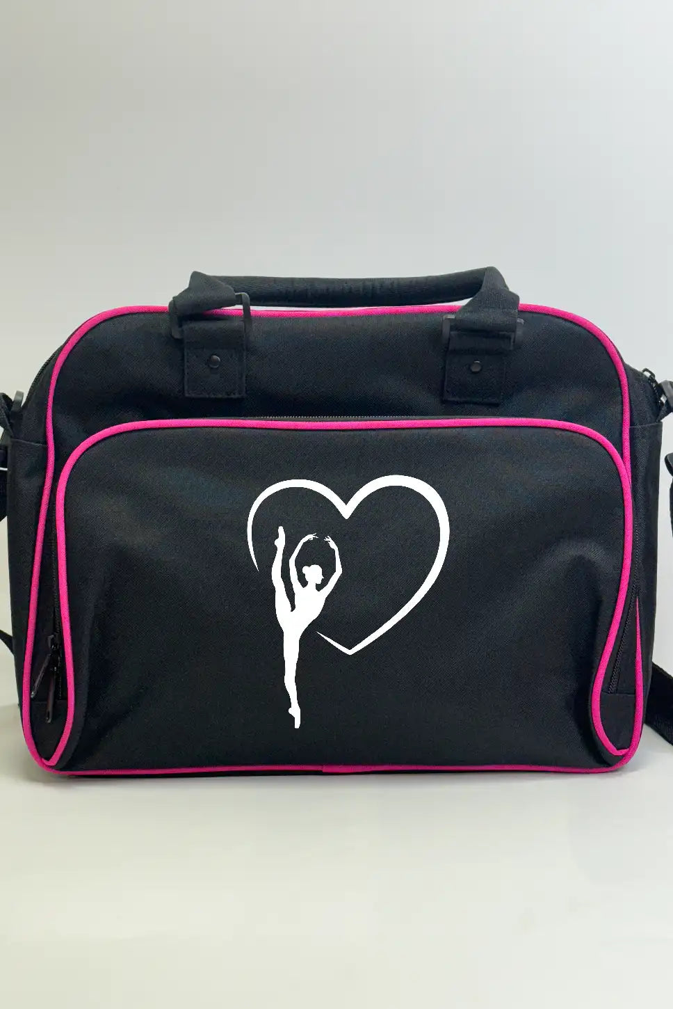 Wir präsentieren die Balletttasche Danceline Herz-Ballett von Danceline: eine stilvolle schwarze Reisetasche mit elegantem rosa Rand, verziert mit der weißen Silhouette einer Ballerina, die ihre Arme anmutig vor einem Herzumriss ausstreckt. Diese vielseitige Tasche verfügt über zwei praktische kurze Griffe und einen abnehmbaren Schultergurt für müheloses Tragen.
