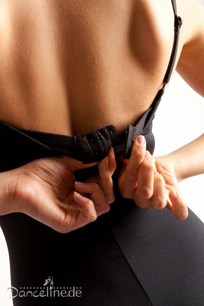 Eine Person im Capezio Ballettanzug SE1020W Bratek mit integriertem BH ist von hinten zu sehen und passt den Haken- und Ösenverschluss an. Die Hände konzentrieren sich auf das Schließen des Rückenverschlusses. In der unteren linken Ecke ist das Logo „Danceline.de“ zu sehen.