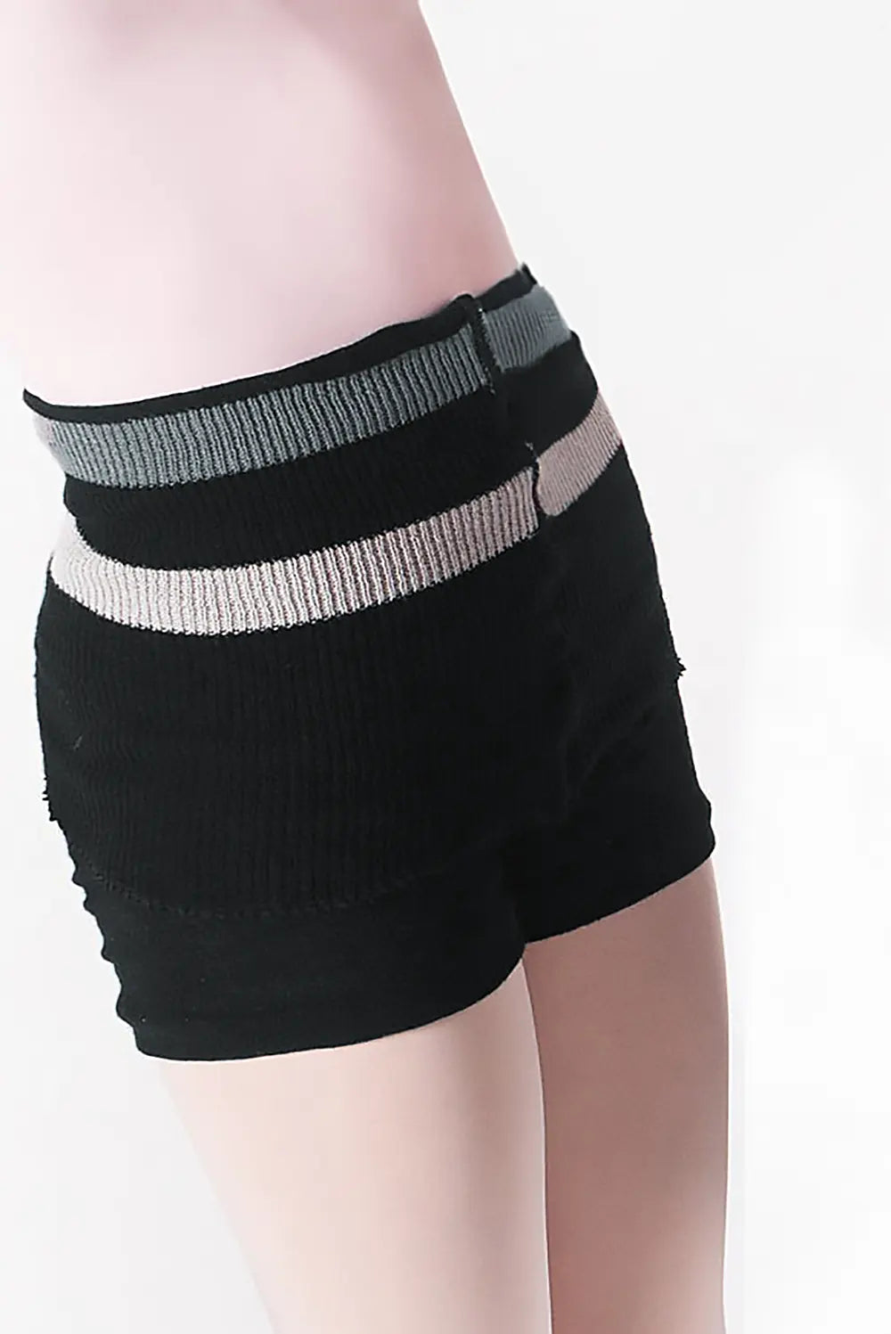 Eine Person trägt die Wärmeshort Intermezzo 5216 von Dance Line, aus schwarzem Strickstoff mit waagerecht grau-weiß gestreiftem Bund, und steht seitlich vor einem einfarbigen Hintergrund.