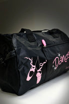 Die Balletttasche Sansha KBAG2 von Dance Line ist eine schwarze Tanztasche mit rosa Ballettschuhen und dem Wort „Dance“ auf der Seite. Sie verfügt über einen rosa Reißverschluss und schwarze Griffe, alles vor einem neutralen Hintergrund.